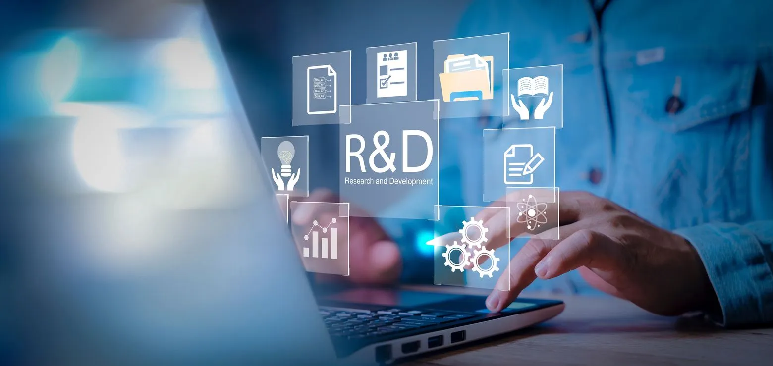 Person typing on a laptop with holographic icons related to research and development, including graphs, documents, and lightbulbs.