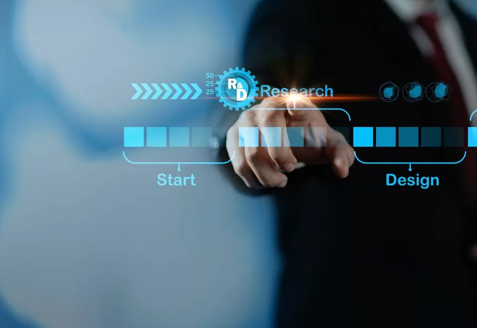 Businessman pointing at a virtual interface with stages labeled "Start," "Research," "Design," and "Develop" against a blurred blue background.