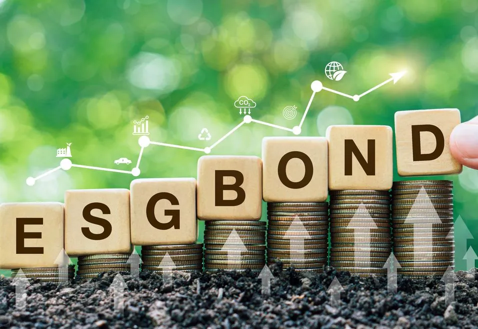 Wooden blocks spelling "ESG BOND" on stacked coins with growth icons and a green background, symbolizing sustainable investment growth.